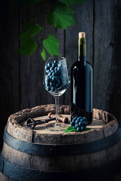 Red wine in bottle and grapes in glass. Wine and a glass on a wooden barrel.  - Φωτογραφία, εικόνα