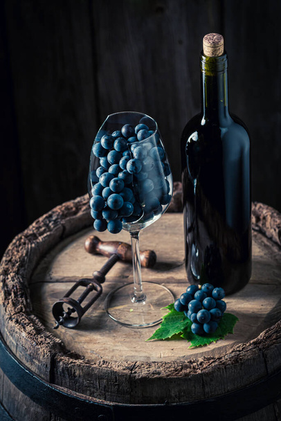 Czerwone wino i ciemne winogrona. Wino i szklanka na drewnianej beczce.  - Zdjęcie, obraz
