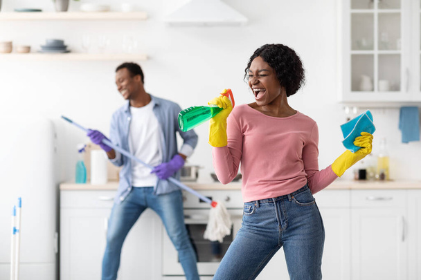Joyful black lady using spray as microphone, singing while cleaning - Фото, изображение