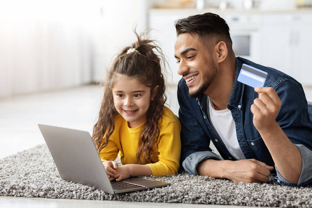 Feliz árabe papá y su hija con ordenador portátil y tarjeta de crédito de compras en línea - Foto, Imagen