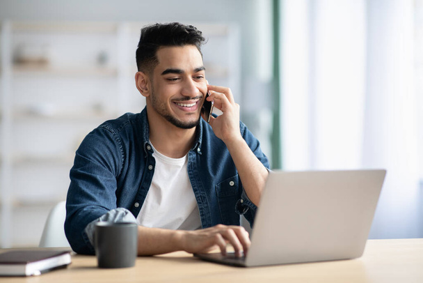 Successful middle-eastern guy talking on phone while working at home - Foto, Bild