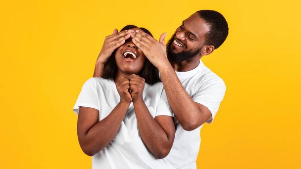 Szczęśliwy czarny mężczyzna robi niespodziankę dla jego kobiety, zakrywając oczy - Zdjęcie, obraz