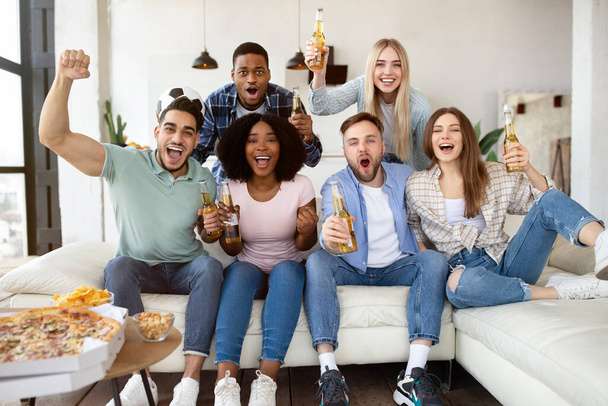 Grupa młodych przyjaciół z przekąskami i piwem oglądających mecz piłki nożnej w telewizji, kibicujących ulubionej drużynie w domu - Zdjęcie, obraz