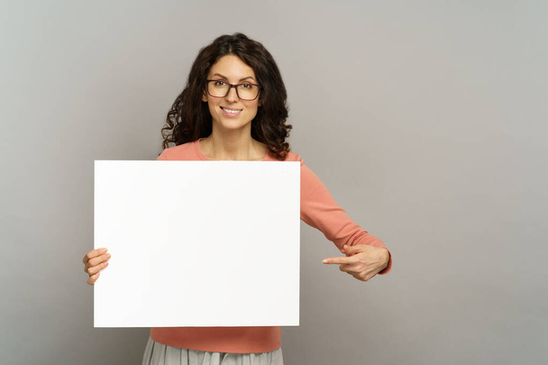 Hymyilevä nainen, jolla on tyhjä juliste lähellä tyhjää kylttiä, näytä mainos mainostaululla tai bannerissa - Valokuva, kuva