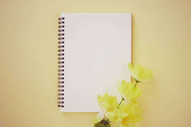 Spiral Notebook or Spring Notebook in Unlined Type and Light Yellow Flower on Pastel Yellow Minimalist Background. Spiral Notebook Mock up on Center Frame in Vintage Tone - 写真・画像