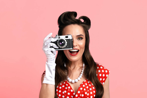 Портрет молодой девушки с ретро камерой, фотографирующей на фоне розовой студии - Фото, изображение