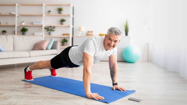 Sportos középkorú férfi edz otthon, álló deszka és jegyzet idő okostelefon - Fotó, kép