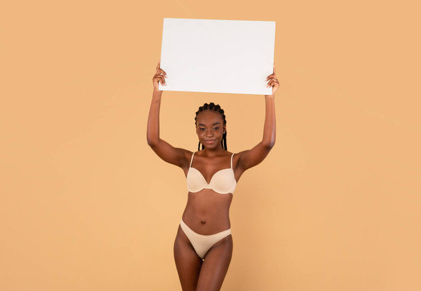 Banner motivacional. Mujer negra con cuerpo ajustado que usa ropa interior que sostiene la placa blanca - Foto, Imagen