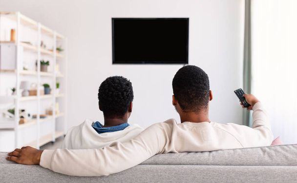 Afro couple watching TV with mockup and using remote controller - Photo, Image