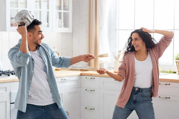 Domestic Fun. Cheerful arab couple playfully fighting in kitchen - Foto, Imagen