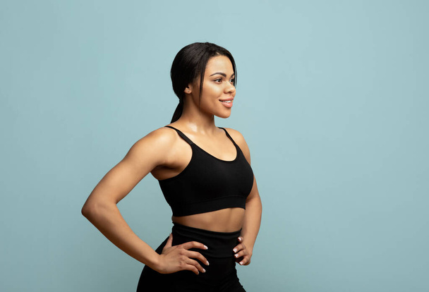 Keep fit. African american woman in sportswear posing and looking aside at free space on blue background, studio shot - 写真・画像