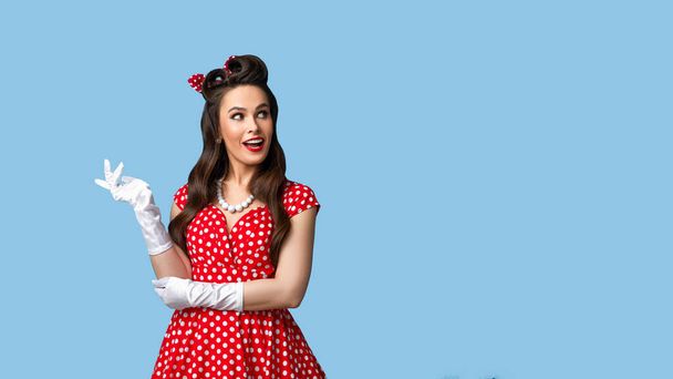 Beautiful young pinup woman in retro vintage outfit looking aside at empty space on blue background, banner design - Фото, изображение