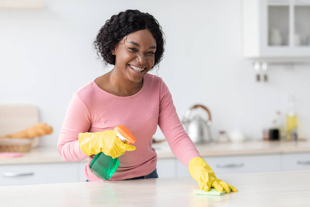 Lächelnde schwarze Dame putzt Küchenmöbel, kopiert Raum - Foto, Bild