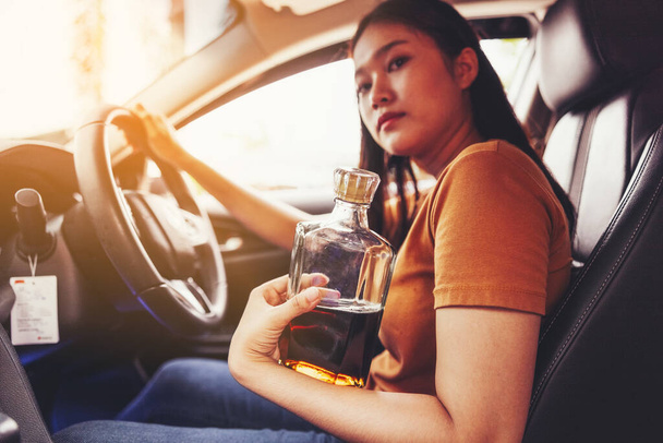 Μεθυσμένη γυναίκα οδηγός στο αυτοκίνητο, μπουκάλι αλκοόλ στο χέρι μιας γυναίκας πίσω από το τιμόνι - μια έννοια της οδήγησης μεθυσμένος - Φωτογραφία, εικόνα