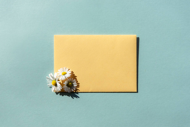Sárga boríték és egy csokor százszorszép kék háttérrel. Lapos laikus sablon üdvözlő kártya, másolás helyet. - Fotó, kép