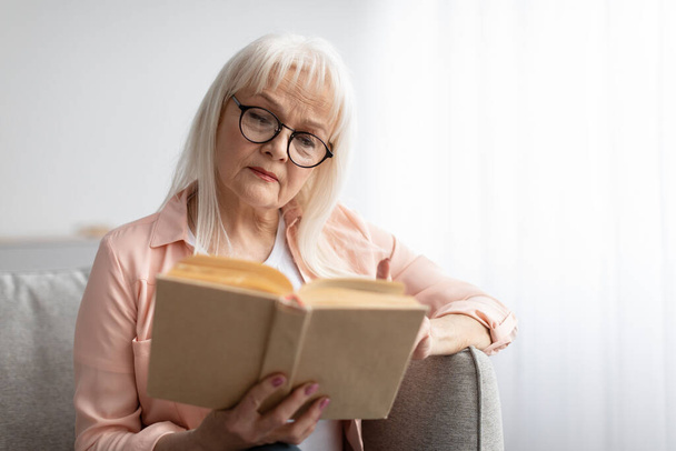 Εστιασμένη ώριμη γυναίκα σε γυαλιά διαβάζοντας βιβλίο - Φωτογραφία, εικόνα