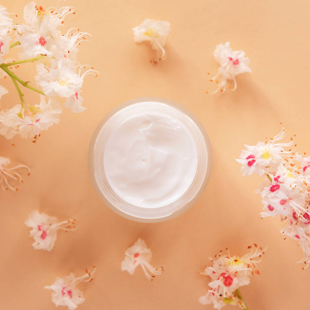 Witte crème pot en Paardenkastanje bloemen op beige achtergrond. Natuurlijke organische cosmetica concept. Bovenaanzicht, vlak lay. - Foto, afbeelding