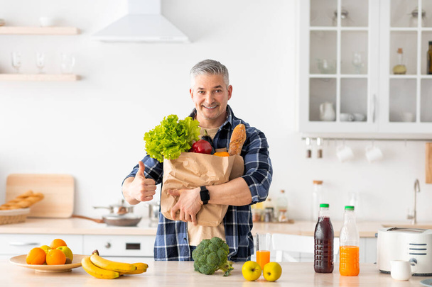 Щасливий старший чоловік жестикулює великий паперовий мішок, повний здорових овочів і продуктів харчування
 - Фото, зображення