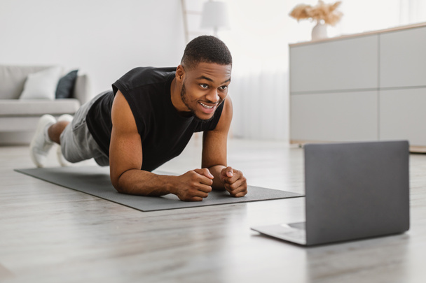 Black Guy doet Elbow Plank Oefening bij Laptop Training Binnenshuis - Foto, afbeelding