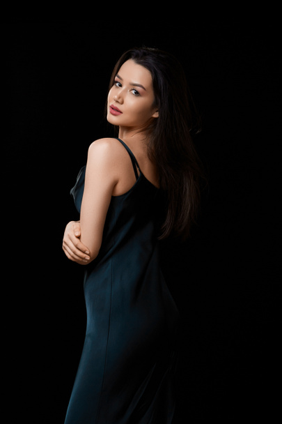 young woman in dark blue dress . on a black isolated background.she touches her face with her hand. it stands half-turned. - Foto, afbeelding
