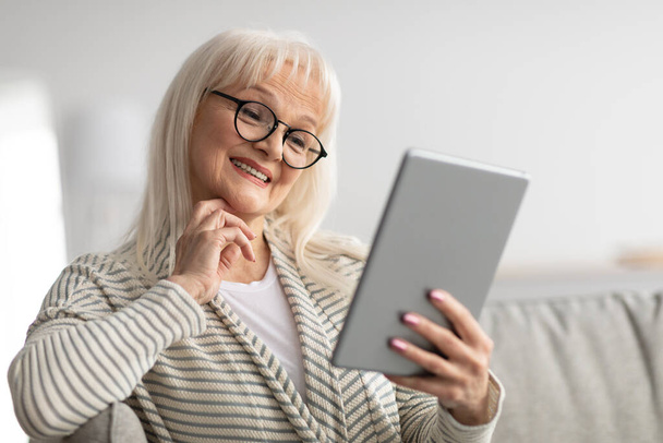 Usmívající se starší žena pomocí tablet sedí na gauči - Fotografie, Obrázek