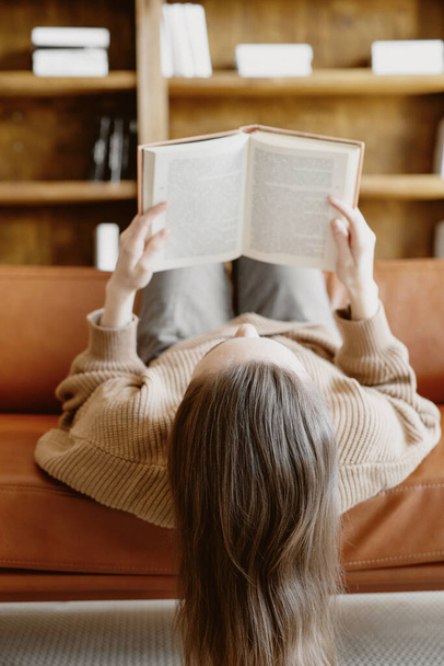 Brunette woman reading a book on the sofa lying upside down. - Foto, afbeelding