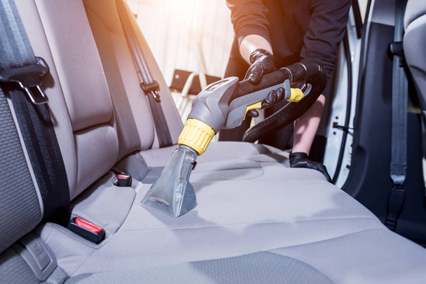 Worker cleans car interior with vacuum cleaner - Foto, afbeelding