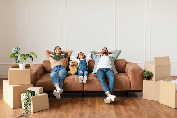 Family relaxing on couch in new home with cardboard boxes - Photo, Image