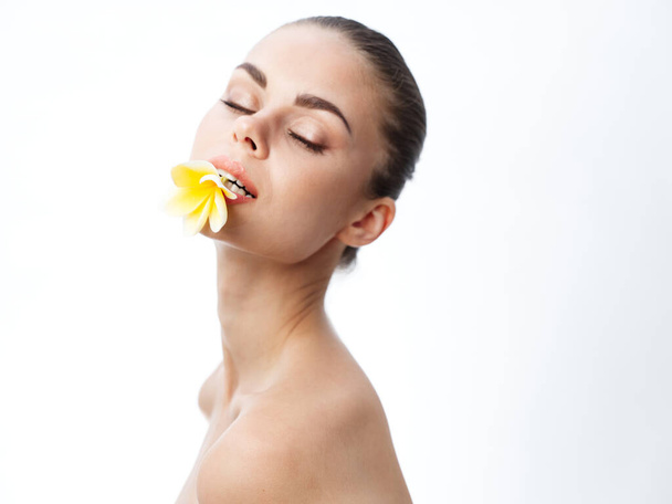 aantrekkelijke vrouw met blote schouders houden gele bloem in haar lippen  - Foto, afbeelding