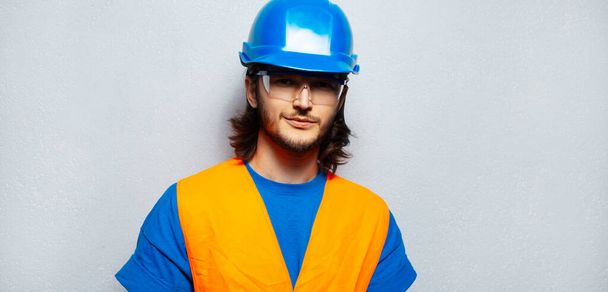 Studio portrait of young confident man, construction worker engineer wearing safety equipment on background of grey textured wall. Panoramic banner view. - Foto, Imagem