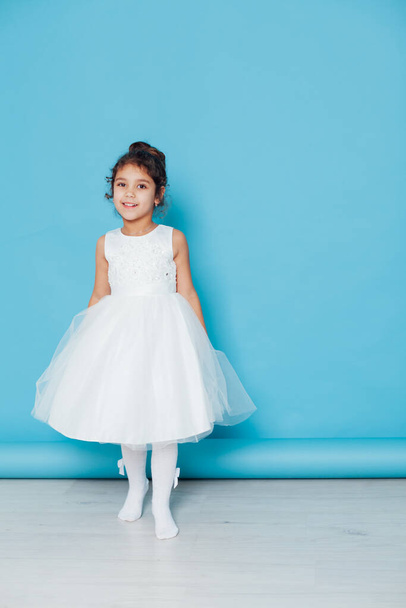 Beautiful little girl dances to the song in a white dress on a blue background - Foto, afbeelding