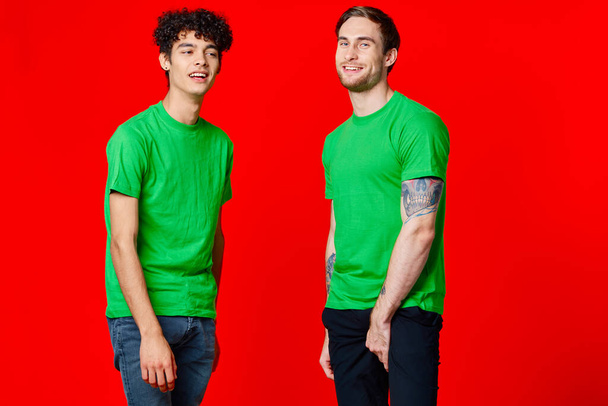 Yeşil tişörtlü iki arkadaş eğlenceli iletişim kırmızı arka plan - Fotoğraf, Görsel
