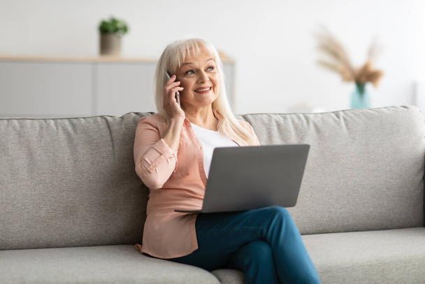 Smiling mature woman working and talking on phone at home - Photo, Image