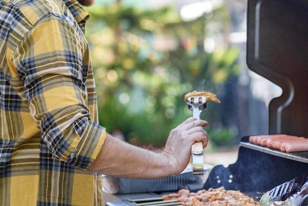 Anonieme man flipt vlees op een barbecue. - Foto, afbeelding