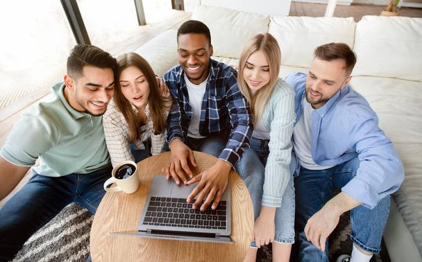 Positive multiethnic friends using laptop at home, making video call, watching movie together, browsing internet - Foto, Imagem