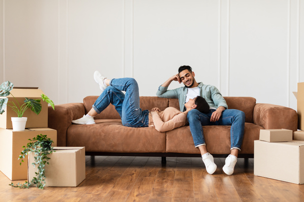 Family relaxing on couch in new home with cardboard boxes - Photo, Image