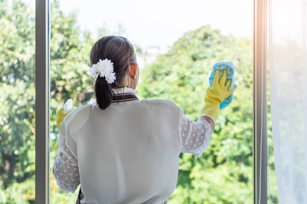 Happy Asian senior female woman using spray bottle and cloth to clean window glass - Zdjęcie, obraz
