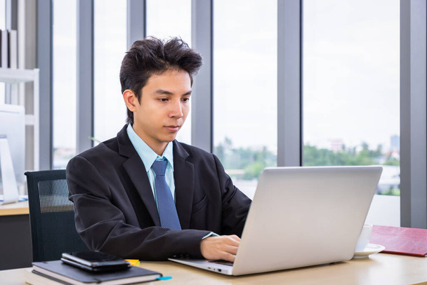 Joven hombre asiático sentado en el escritorio de la oficina y trabajando con el ordenador portátil. Empresario o sueldo vida de hombre. - Foto, Imagen