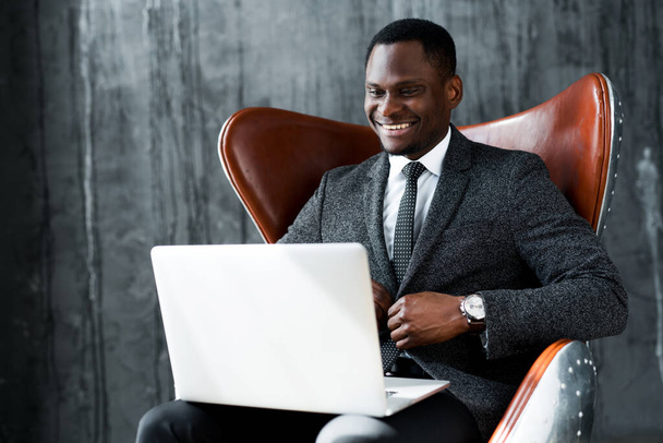 Smiling african american businessman sitting on chair and holding business conference on laptop - Photo, Image