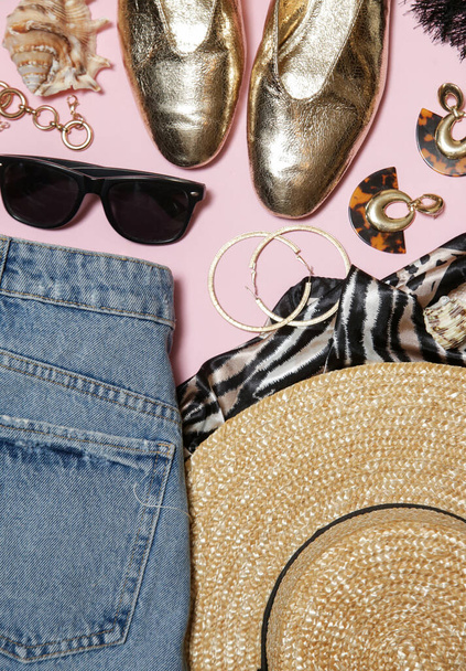 Zomer outfit op roze achtergrond, blauwe jeans, strohoed en gouden accessoires. Modieuze damesartikelen voor het zomerseizoen. - Foto, afbeelding