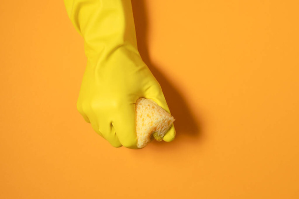 een hand in een rubberen handschoen houdt een reinigingsspons vast. monochrome fotografie in gele kleuren. - Foto, afbeelding