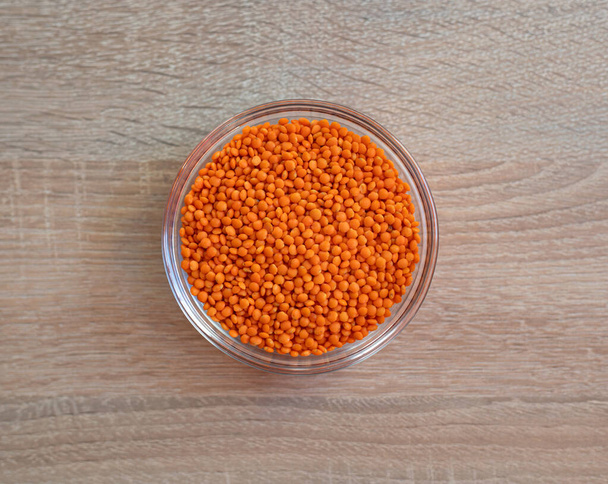 木のテーブルの上に生の穀物の赤いレンズ豆のボウル - 写真・画像