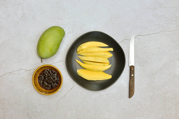 Πράσινο μάνγκο και έτοιμο να φάει σε μαύρο πιάτο με γλυκιά σάλτσα ψαριού στο τραχύ τσιμεντένιο πάτωμα, ταϊλανδέζικο δημοφιλές φαγητό, φρέσκα μάνγκο βιολογικά και φρούτα υψηλής βιταμίνης C για υγιή - Φωτογραφία, εικόνα
