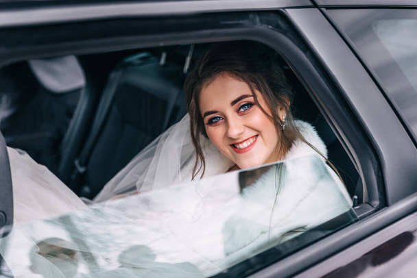 ślub: szczęśliwa piękna panna młoda w samochodzie z fryzury i jasny makijaż. Kobieta w białej sukience w dniu ślubu czeka na pana młodego i pozowanie. Koncepcja szczęścia i miłości. - Zdjęcie, obraz