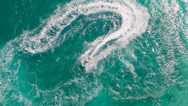 Αεροφωτογραφία του τζετ σκι ή σκάφος που σχεδιάζει ένα σχήμα στη θάλασσα ωκεανό τιρκουάζ νερό. Περιπέτεια υπαίθρια ακραία δραστηριότητα αναψυχής κατά τη θερινή περίοδο. Τρόπος ζωής - Φωτογραφία, εικόνα