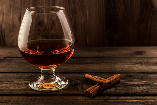 Glass of brandy with cinnamon stick on a wooden table.  - Foto, Imagen
