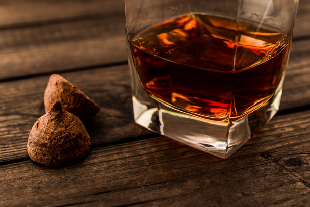 Glass of brandy with a couple chocolate truffles on an old wooden table - Photo, image