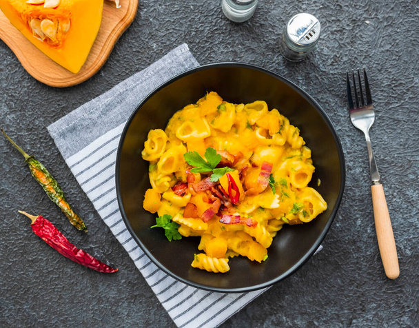 Pasta with pumpkin, fried bacon and hot peppers in a black plate on a dark concrete background. Pasta recipes. Italian food. - Foto, immagini