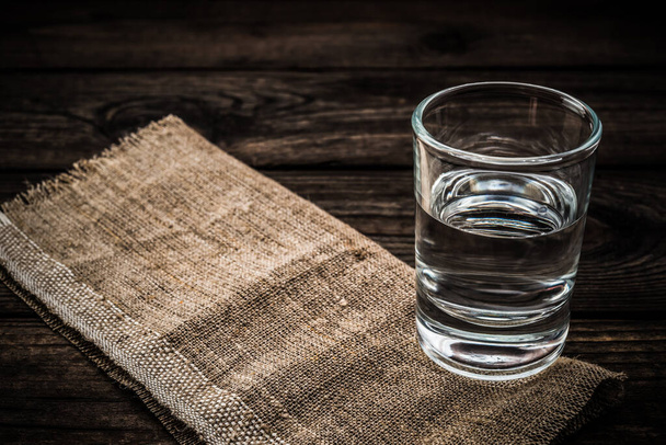 Shot of vodka with piece of cloth on an old wooden table. Close up view - Fotó, kép