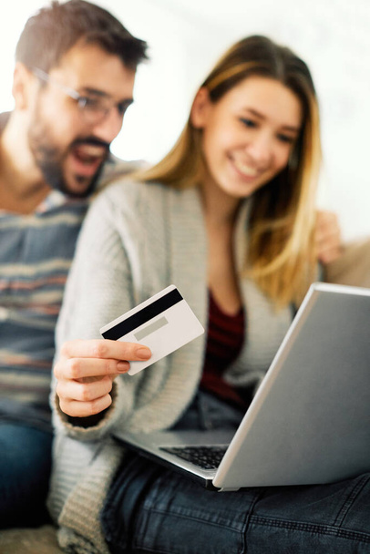 Šťastný pár nakupování on-line s jejich kreditní kartou a notebookem v obývacím pokoji - Fotografie, Obrázek